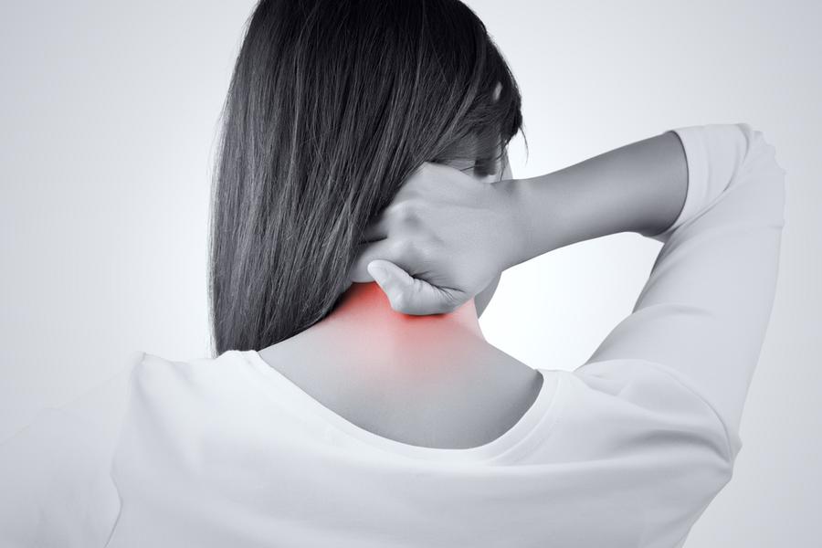 梅田で寝違えによる首の激痛に悩み、後ろから首の付け根を痛そうに押さえる女性。深層筋の癒着と関節のロックを表現。