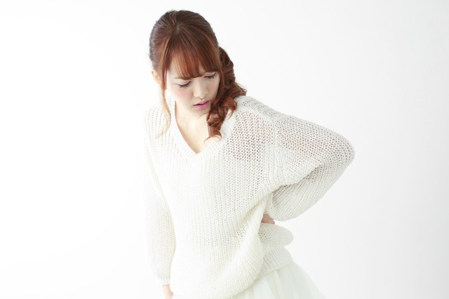 重度の腰痛により、椅子から立ち上がる際に鋭い痛みを感じ、腰を強く押さえて顔をしかめている人物のイメージ