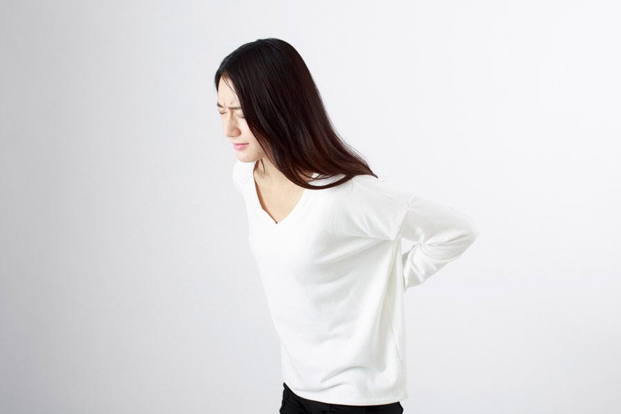 腰椎すべり症で痛そうに腰を押さえている女性のイメージ