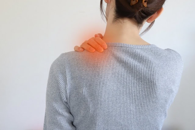 頚肩症候群で首と肩が痛む部分に手をあてる女性のイメージ画像