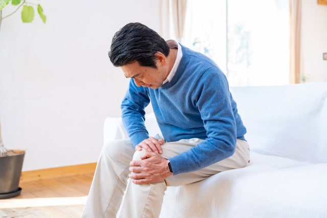 変形性膝関節症による膝の痛みで膝男押さえて座り込んでいる男性のイメージ画像