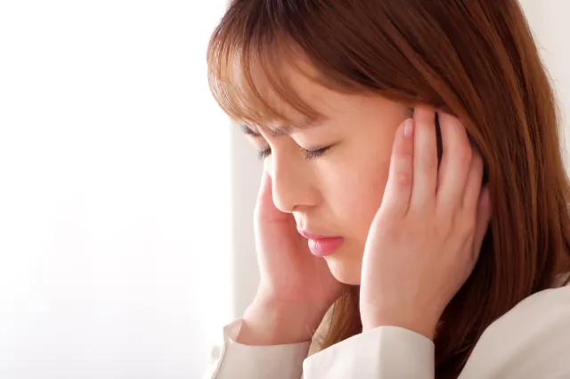 突発性難聴で耳を押さえる女性のイメージ画像