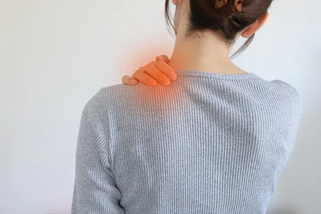 頚肩症候群で首と肩が痛む部分に手をあてる女性のイメージ画像
